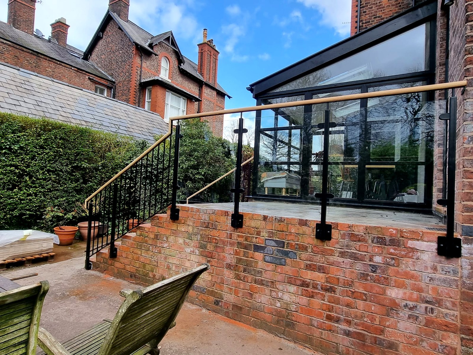 Powder-coated steel and glass balustrade with iroko handrail beside a black-framed glass extension, Manchester